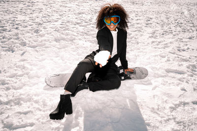 African american woman with goggles and a snowboard on a snowy mountain during winter