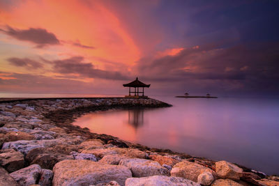 Rocky walkway leading towards gazebo by sea during sunset