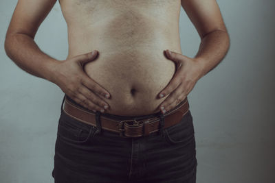 Midsection of shirtless woman against gray background
