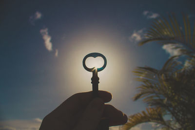 Low angle view of hand holding silhouette tree against sky