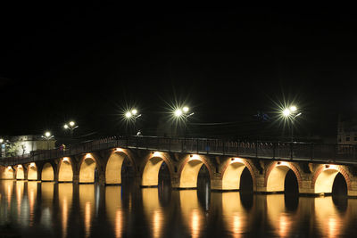 Illuminated bridge over water in city against sky at night