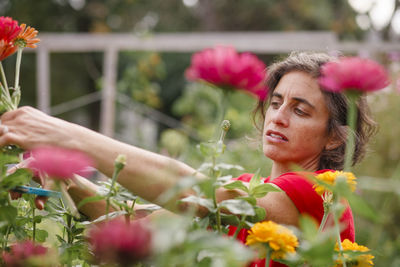 A woman stands among wildflowers cutting stems with a scissors