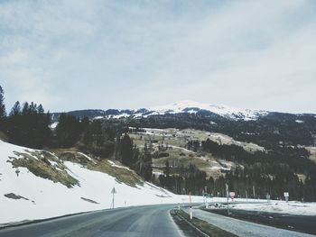 Road by mountains against sky during winter