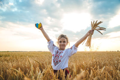 Portrait of girl holding heart shape with crops at field