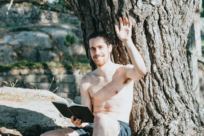 Portrait of shirtless man sitting on tree trunk