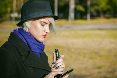 Young woman using mobile phone while smoking at park