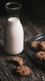 Close up of bitten chocolate chip cookie and a bottle of milk on a plate with crumbs simple snack
