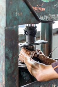 Cropped image of man holding metal on machinery