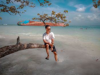 Full length portrait of young man at beach against sky