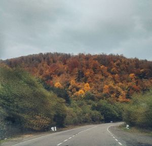 Road amidst trees against sky during autumn