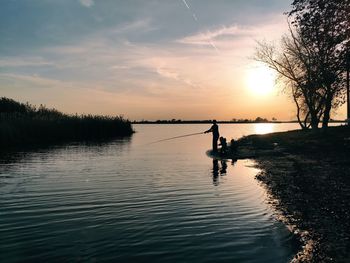 Silhouette person by lake against sky during sunset