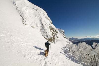Full length of man with dog climbing on snowcapped mountain against sky