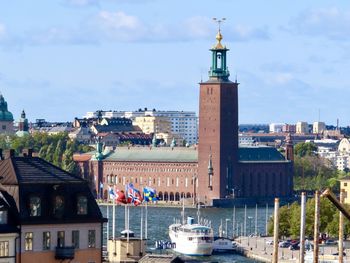 View of buildings by river in city against cloudy sky