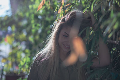 Smiling young woman with hand in hair by plants during sunny day