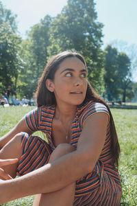 Beautiful young woman looking away while sitting in park