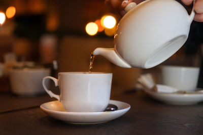 White cup with teapot. hand pours tea into a pot on blurred background. concept of a cozy pastime