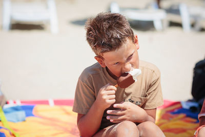 Handsome boy sitting on the beach and eating ice cream
