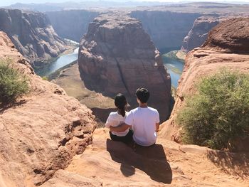 Rear view of couple sitting on rocky cliff against horseshoe bend