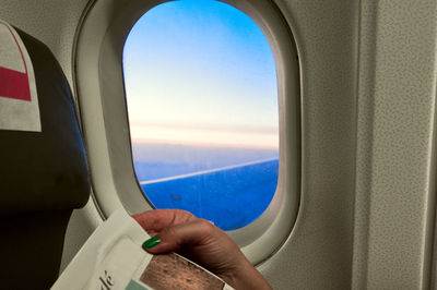 Cropped hand of woman holding paper against window in airplane