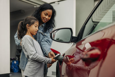 Mature mother assisting daughter charging electric car near house