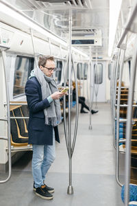 Vertical photo of man with glasses and wireless headphones rides in the subway train. 