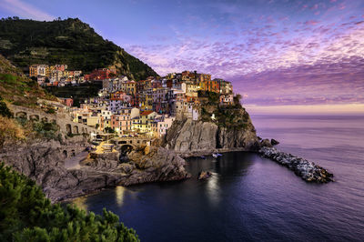 Townscape and mountains by sea against sky during sunset