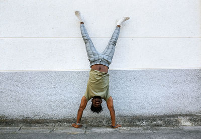 Mid adult man doing handstand on footpath against wall in city