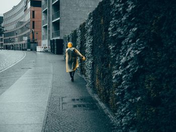 Rear view of woman in raincoat walking at sidewalk