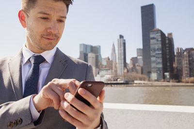 Portrait of a young businessman using his smartphone on a rooftop overlooking the city