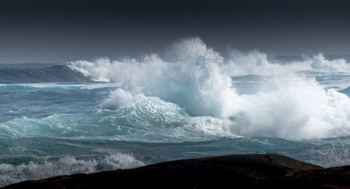 Sea waves splashing on shore against sky