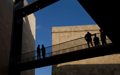 Low angle view of silhouette people walking on bridge against sky