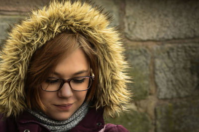 Smiling young woman wearing fur hooded shirt against wall