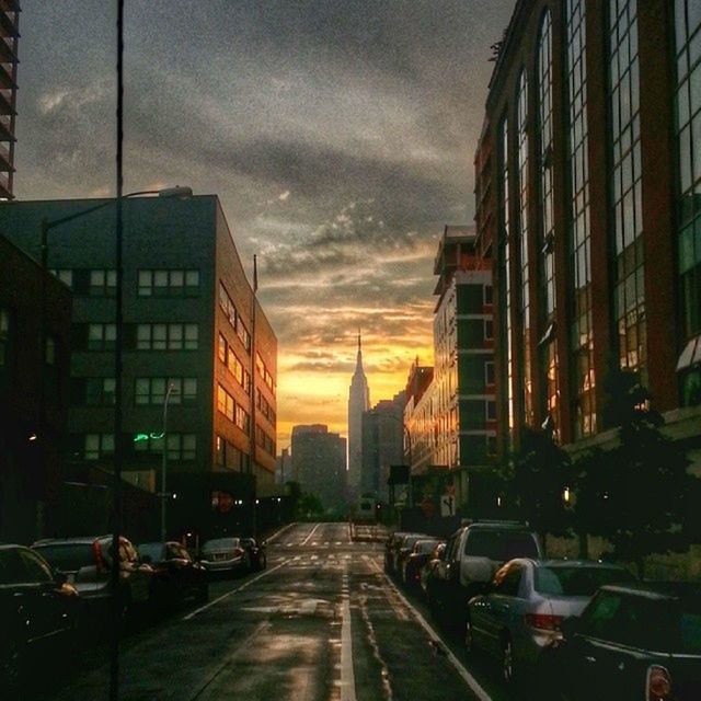 building exterior, architecture, transportation, built structure, city, car, mode of transport, land vehicle, sky, street, sunset, cloud - sky, road, building, the way forward, city life, city street, diminishing perspective, cloudy, residential building