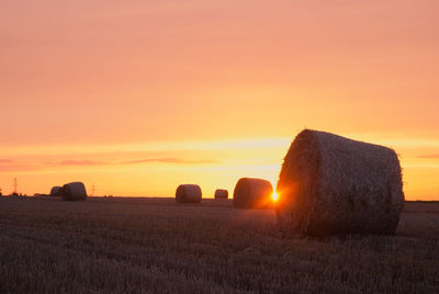 Hay bales on field against sky during sunset