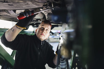 Female mechanic examining car with hammer in auto repair shop