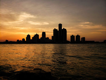 Silhouette buildings by sea against sky during sunset