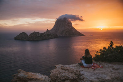 Woman sitting against sea during sunset