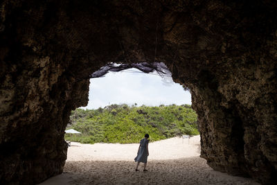 Rear view full length of woman walking in cave at beach