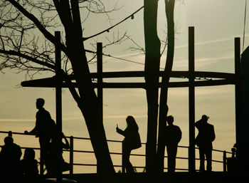 Silhouette people standing by railing against sky during sunset