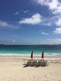Deck chairs on beach against sky