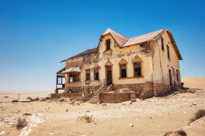 Old building on beach against clear blue sky