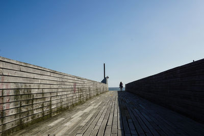 Man walking on footpath against clear blue sky