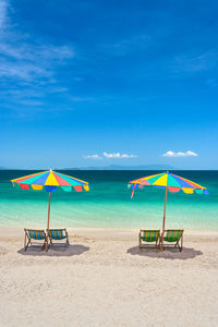 Deck chairs and parasols at beach against blue sky