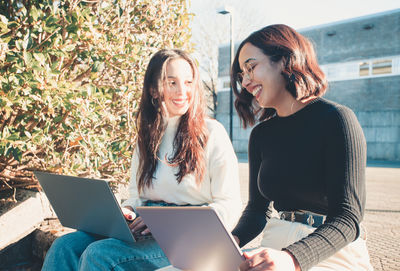 Happy businesswomen with laptops talking on sunny day