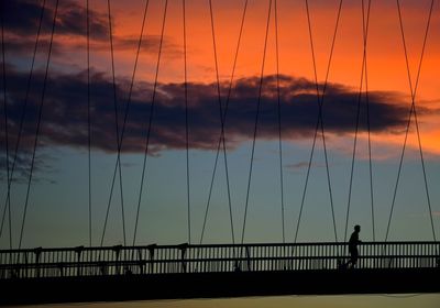 Silhouette bridge over sea against sky during sunset