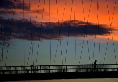 Silhouette man running on bridge against sky during sunset