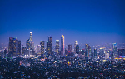 Illuminated buildings in city against blue sky