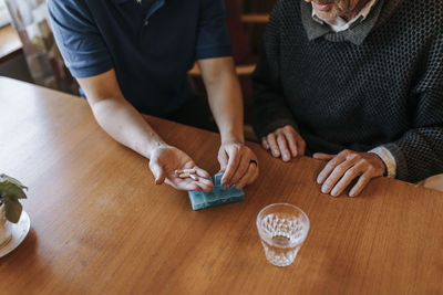 High angle view of female caregiver helping senior man while having medicines at home