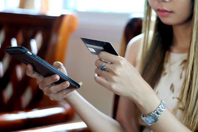 Midsection of woman holding credit card while using mobile phone