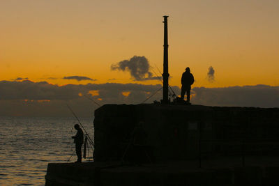 Silhouette men fishing in sea against sky during sunset